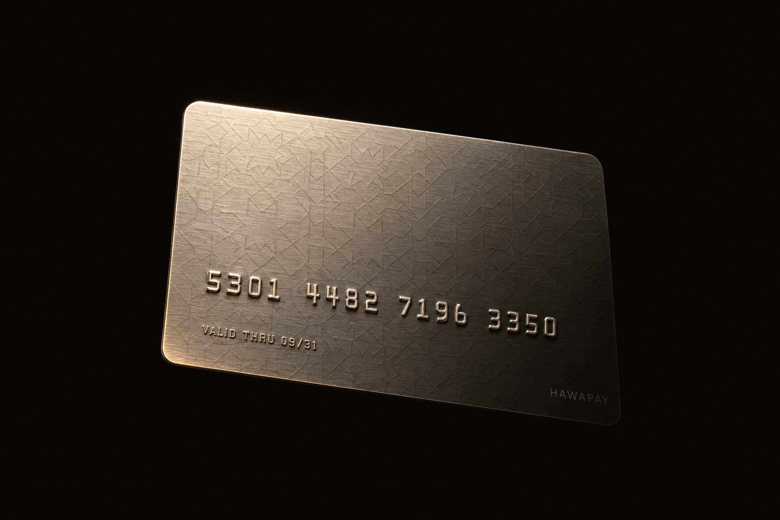 A blank dark metal payment card standing on edge, engraved arabesque catching the light on one corner